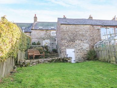 A garden with a bench, steps, and a greenhouse at Englewood Cottage in Hexham