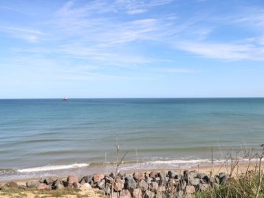 A view of the ocean with a boat in the distance and rocks at the shore