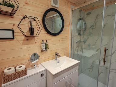 A bathroom with a sink, shower, and wall shelves at Bluebelle - Crossgate Luxury Glamping, Hartsop