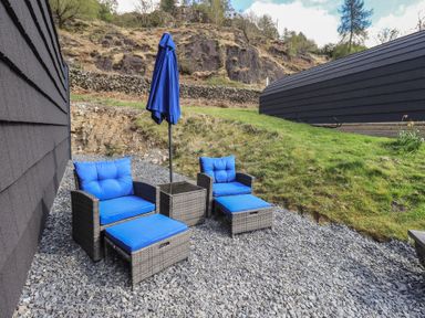 An outdoor seating area with blue cushioned chairs and umbrella at Bluebelle - Crossgate Luxury Glamping Hartsop