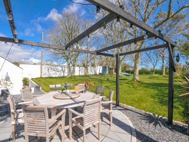 An outdoor dining table surrounded by chairs in a garden at The Cowshed in Portscatho