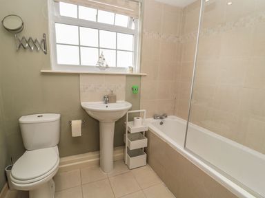 A bathroom with a sink, toilet, bathtub, and shelf at Shepherds Nook in Chathill