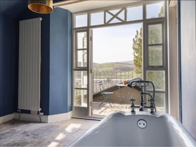 A bathroom with a bathtub and view to an outdoor balcony at Plas Dolguog in Machynlleth