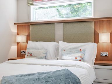 A bedroom with a bed, pillows, and a window at Fern View -Kelling Heath Holiday Park in Weybourne near Sheringham