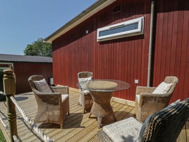 A patio area with wicker furniture and a glass table at Chalet 23 Erw Porthor Tywyn
