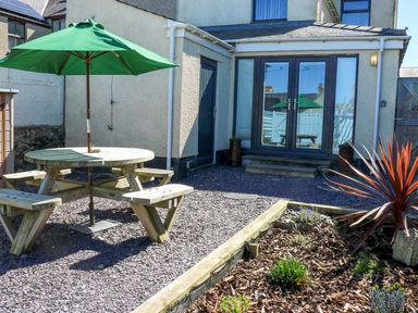 A garden with a table and benches under an umbrella at Rhiwlas in Rhosneigr