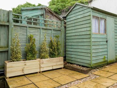 A garden with a shed and plants in planters at Cotswolds Cozy Cottage Retreat - pet friendly, Finstock