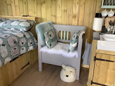 A bedroom with a bed, cushions, a bench and a sink at The Shepherds Hut at Hafoty Boeth, Corwen
