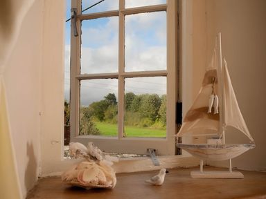 A window view with a sailboat decoration and bird figurine at Quiet cottage on the rural edge of Brixham
