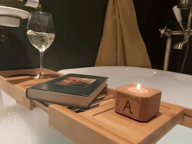 A bathtub with a wine glass, book, and candle at Quiet cottage on the rural edge of Brixham