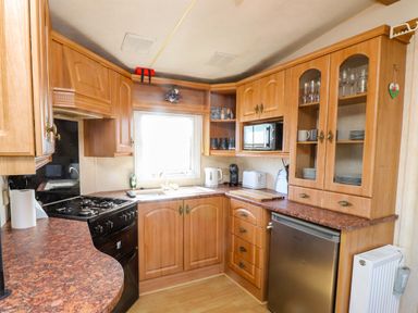 A kitchen with cabinets, sink, stove, and appliances at Caravan at Argraig Llanrhyddlad near Cemaes Bay