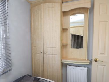 A bedroom with a wardrobe and mirror at Caravan at Argraig near Cemaes Bay