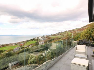 A balcony with seating overlooking the sea and houses at Briar Bank in Barmouth