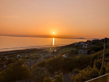 A sunset over the sea with hills and houses at Briar Bank in Barmouth