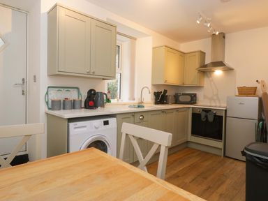 A kitchen with cabinets, appliances, and a dining table at Bobtail Cottage in Kendal