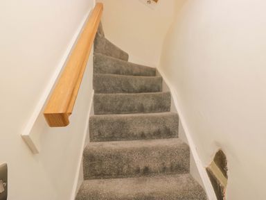 A staircase with a wooden handrail at Bobtail Cottage in Kendal