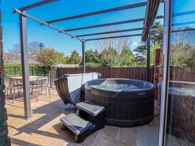 An outdoor patio with a hot tub and dining table at Elwy Cottage St Asaph