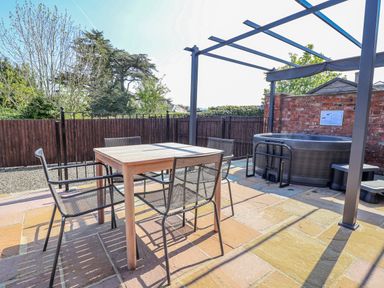 An outdoor area with a table, chairs, and a hot tub at Elwy Cottage in St Asaph