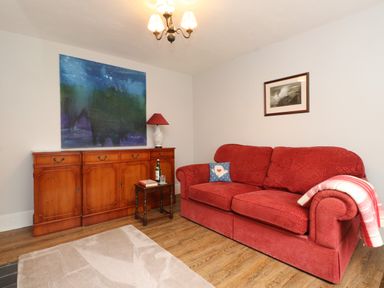 A living room with a red sofa and a painting at 3 Tre Felin in Llandygai near Bangor