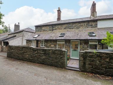 A cottage with a stone wall and door at 3 Tre Felin in Llandygai near Bangor