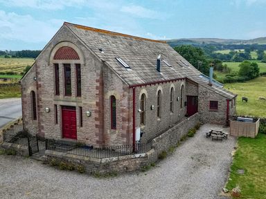 An exterior view of a building with a red door and windows at Kaber Chapel near Kirkby Stephen