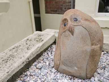An owl sculpture made of stone surrounded by gravel at The Hideaway in Whitby