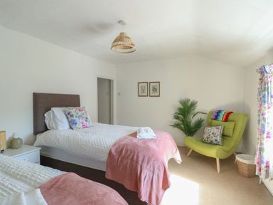 A bedroom with two beds and a green chair at Castle Gardens Apartment Beaumaris