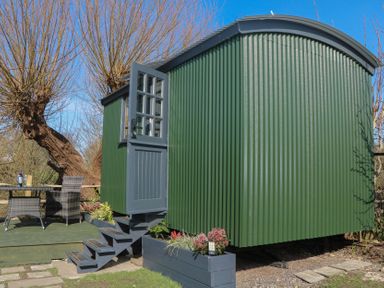 A green shepherd's hut with outdoor seating area at Salt Haven Shepards Hut Pevensey