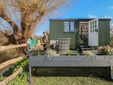 An outdoor view of a shepherd's hut with a chair and flower bed at Salt Haven Shepards Hut Pevensey