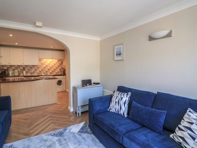 A living room with a blue sofa and kitchen area at 6 Dartmouth House in Dartmouth