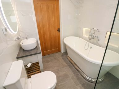 A bathroom with a bathtub, toilet, sink and wooden door at Dairy Cottage Oxwich