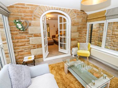 A conservatory with a sofa and glass coffee table at Stone Lodge near Haltwhistle
