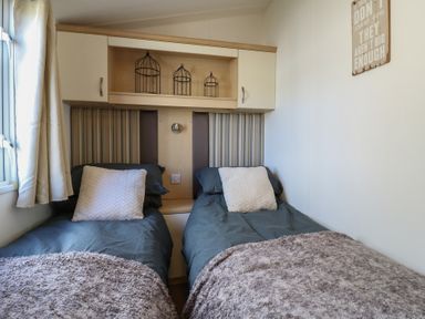 A bedroom with two single beds and a shelf with decorative items at 2 bed Caravan Stowmarket