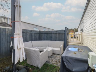 An outdoor seating area with a circular couch and umbrella at 2 bed Caravan Stowmarket