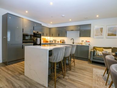 A kitchen with a grey island and bar stools at 2 Glan Yr Aber in Colwyn Bay