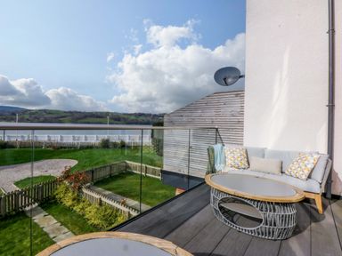 A balcony with a couch and coffee table overlooking a garden at 2 Glan Yr Aber in Colwyn Bay