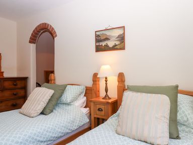 A bedroom with two beds and a nightstand with a lamp at The Cottage in Sampford Courtenay