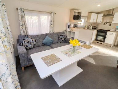 A living room with a sofa and kitchen area at Gardeners Lodge