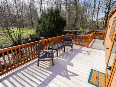 An outdoor deck with chairs and a welcome mat at Gardeners Lodge
