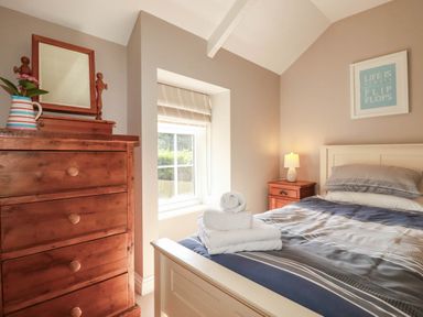 A bedroom with a bed, dresser, towel, and lamp at Bryher Cottage in St Mawgan