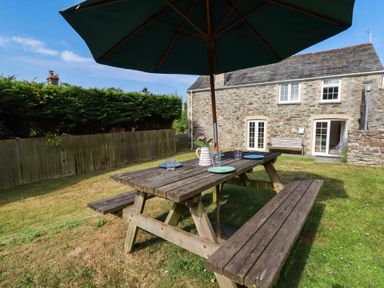 A picnic table with an umbrella and pitcher in the garden at Bryher Cottage St Mawgan