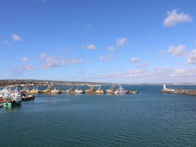 A view of fishing boats at the harbor with a lighthouse at Wootton Gray in Penzance