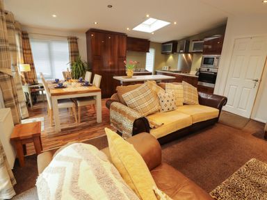 An open plan living area with a kitchen and dining table at Jodene Lodge, Bowness-On-Windermere