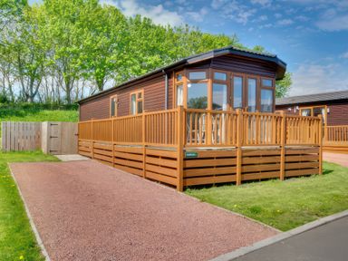A lodge with a deck and surrounding trees at Pet-friendly lodge with hot tub near the coast