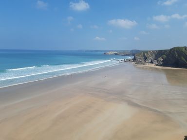 A beach with waves and cliffs in the distance at Surf-ready apartment with sea views in town