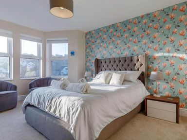 A bedroom with a bed, armchairs, and windows at tbc