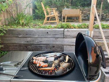 A grill with seafood cooking at a backyard with patio furniture at tbc