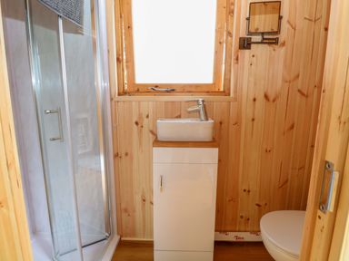 A bathroom with a shower, sink, toilet, and wooden walls at Hazel