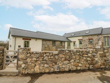 An outdoor view of a stone house and wall at Barley Cottage in Oxwich