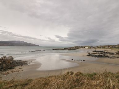 A beach with rocks and houses under a cloudy sky at 2 Ard an Chuain Dunfanaghy